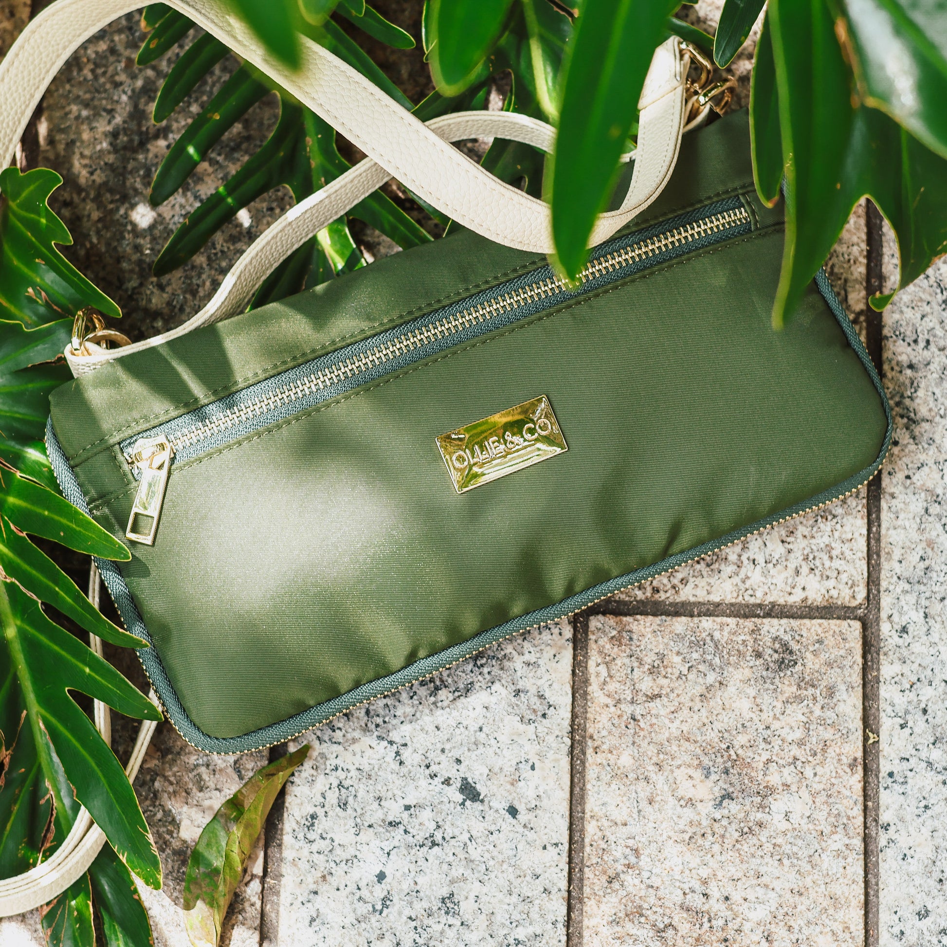 Green handbag with a visible brand logo on a stone surface with green leaves.