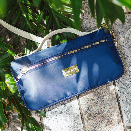 Blue handbag with a visible brand logo on a textured surface with green leaves in the background